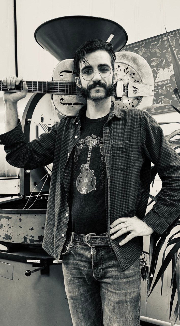 Devin from Lake Wind Coffee holding a resonator guitar in the roastery